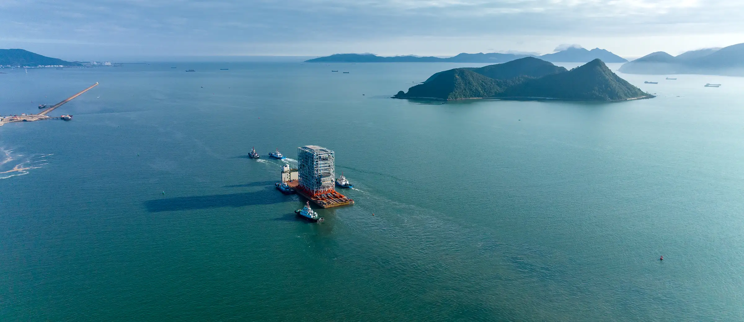Tugboats transporting a large modular structure on a barge through coastal waters