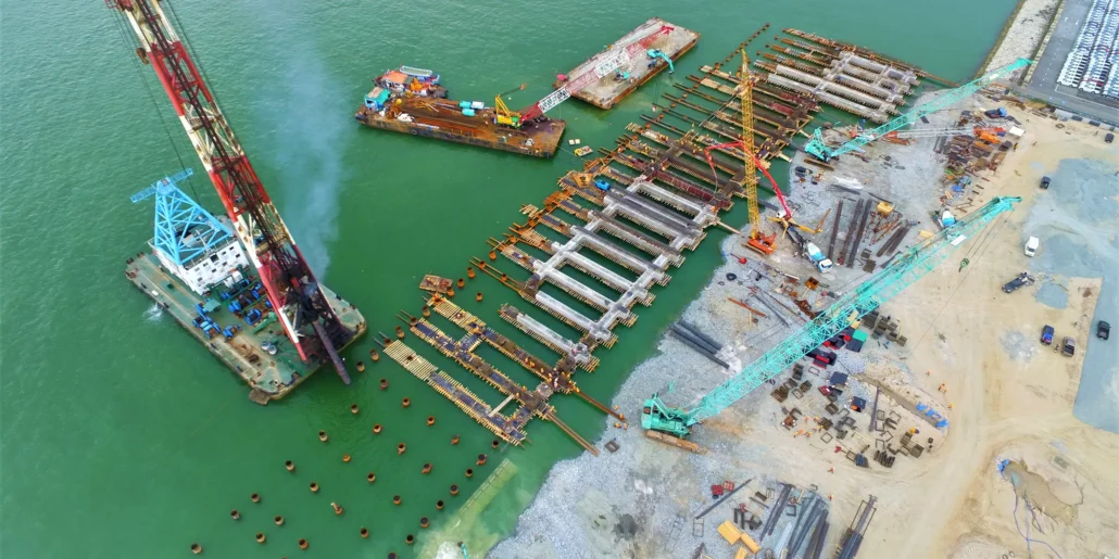 Aerial view of cranes, barges and piles during marine construction beside a quay.