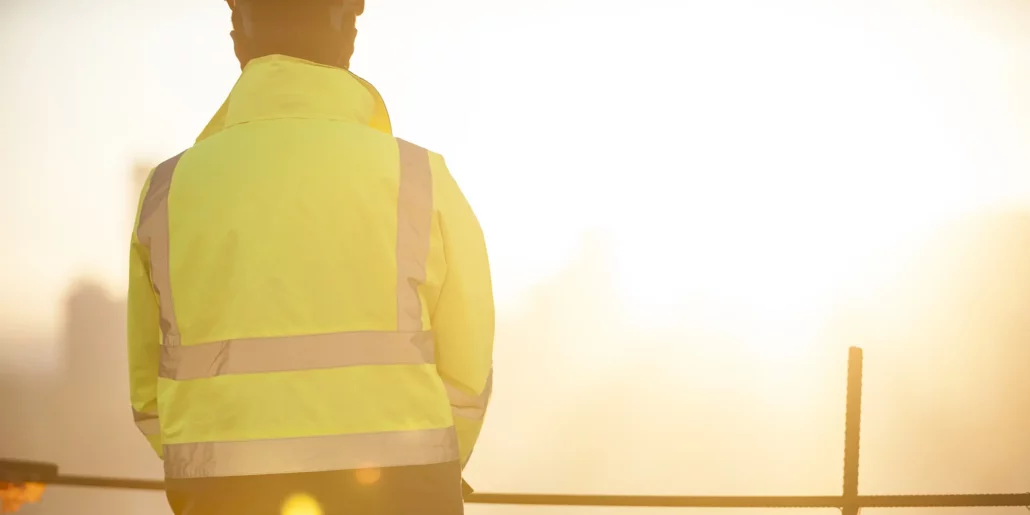 Construction professional in a high-visibility jacket overlooking a site in warm evening light.