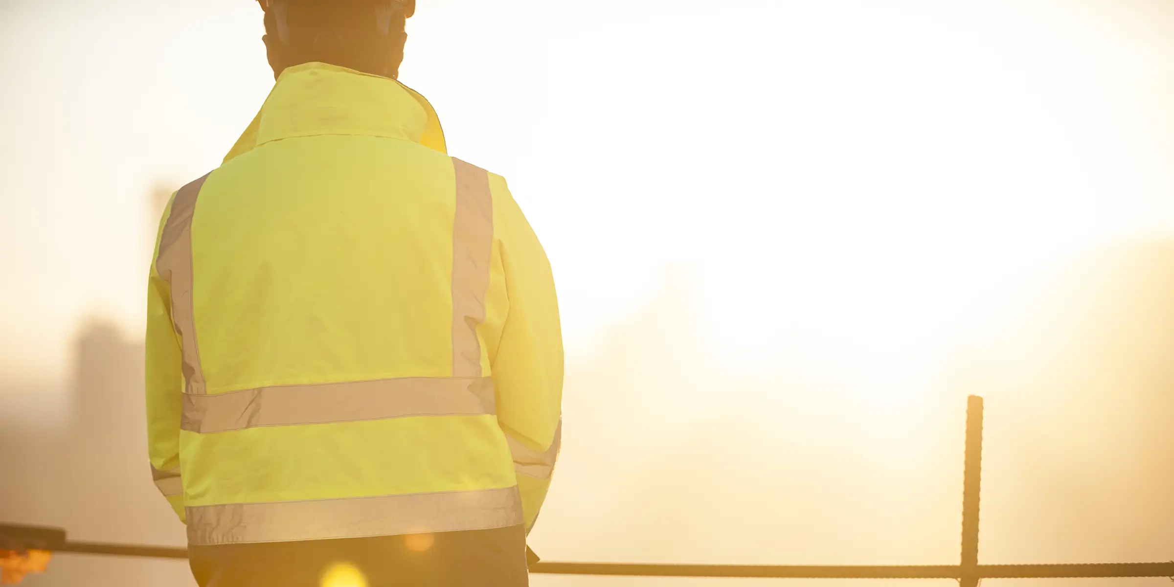 Construction professional in a high-visibility jacket overlooking a site in warm evening light.